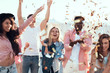 Outgoing males and cheerful women throwing confetti having fun outdoor. Positive comrades spending time together concept