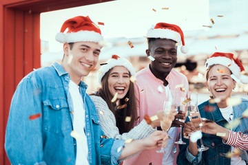 Wall Mural - Portrait of beaming young men and satisfied girls telling while clanging glasses of champagne. They looking at camera. Glad comrades during party concept