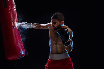 Wall Mural - Bearded male boxer training with punching bag on black background. Male boxer as exercise for the big fight.