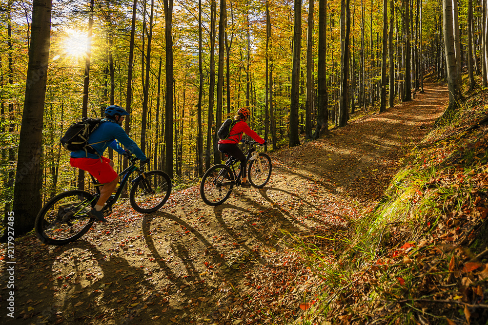 Cycling, mountain biker couple on cycle trail in autumn forest. Mountain biking in autumn landscape forest. Man and woman cycling MTB flow uphill trail. - obrazy, fototapety, plakaty 