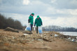 © pressmaster - Two volunteers standing and collecting rubbish to bags on shore