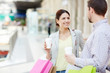 © pressmaster - Adult relaxed woman having coffee with man while standing with paper bags in shopping mall