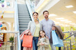© pressmaster - Content parents with shopping bags and charming little girl standing on background of escalator in shopping mall smiling at camera
