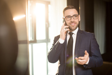 smiling elegant man in suit and glasses having phone call and talking with emotions looking away in 