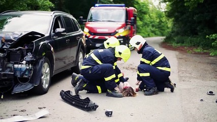 Wall Mural - Firefighters rescuing a young injured woman lying on the road after an accident.