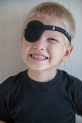 happy blond child with black medical patch occluder on eye