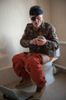 © galitsin - Man with gray hair, beard and mustache in military jacket with laptop sitting on toilet. Man's eye is covered with black medical patch. Dude is infatuated with computer and actively expressed emotions
