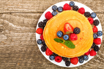 Wall Mural - Pancakes stack with different berries on old wooden background with copy space for your text. Top view. Flat lay