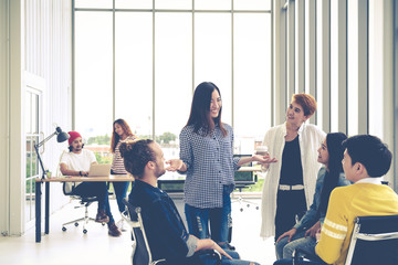 Wall Mural - Group of young multiethnic creative team engaged brainstorm in small meeting while standing, sitting and talking together in modern office. Casual business with teamwork community discussion concept.