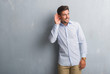 © Krakenimages.com - Handsome young business man over grey grunge wall wearing elegant shirt smiling with hand over ear listening an hearing to rumor or gossip. Deafness concept.