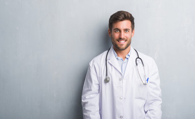 Handsome young doctor man over grey grunge wall with a happy and cool smile on face. Lucky person.