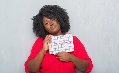 Poster - Young african american woman over grey grunge wall holding menstruation calendar with a confident expression on smart face thinking serious