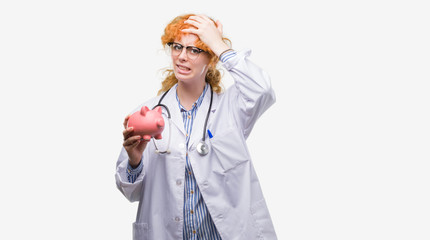 Poster - Young redhead doctor woman holding piggy bank stressed with hand on head, shocked with shame and surprise face, angry and frustrated. Fear and upset for mistake.