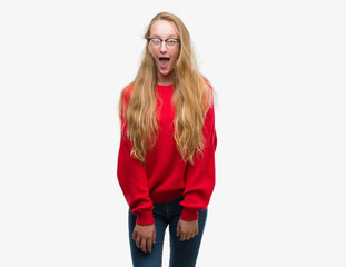 Poster - Blonde teenager woman wearing red sweater afraid and shocked with surprise expression, fear and excited face.