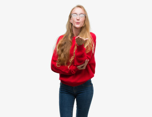 Blonde teenager woman wearing red sweater looking at the camera blowing a kiss with hand on air being lovely and sexy. Love expression.