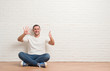 © Krakenimages.com - Young caucasian man sitting on the floor over white brick wall showing and pointing up with fingers number six while smiling confident and happy.