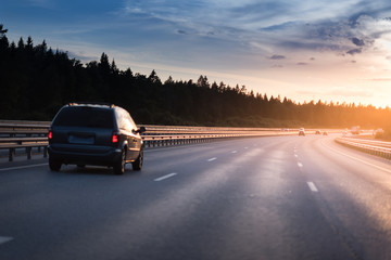 Highway traffic in sunset. minivan on the asphalt road with metal safety barrier or rail. Pine forest on the background