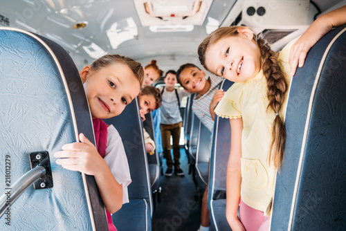 Fotomural group of cute schoolchildren riding on school bus and looking at camera