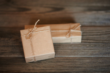 Boxes in craft paper, eco paper on the wooden table. Parcels or gifts tied with twine. Brown paper wrapped gift box with rope bow on a old rustic wood background. Background for your design.