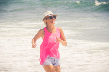 Happy cheerful woman running along the beach against the ocean