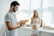 © LIGHTFIELD STUDIOS - smiling pregnant wife with fruits salad and husband with book in kitchen at home