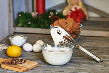 Wall Mural - Bowl with icing,  whisk for whipping eggs, sugar, lemon and  gingerbread  on a old wooden table. Christmas gingerbread.