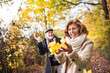 © Halfpoint - Senior couple on a walk in a forest in an autumn nature, holding leaves.