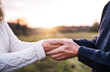 A close-up of holding hands of senior couple in an autumn nature at sunset.