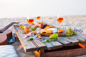 Picnic on beach at sunset in boho style. Romantic dinner, friends party, summertime, food and drink concept