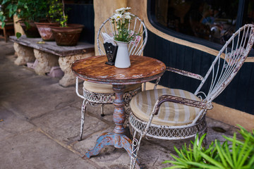 Old white antique wrought iron furniture, shabby chic exterior. Set of round table with flowers and two elegant chairs in the street in the old town. Table on cafe background. Vintage style.  .