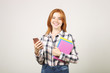 © Evrymmnt - Young beautiful woman with long natural red head wearing checkered flannel shirt holding bunch of notebooks and mobile cell phone, chatting in app, smiling at screen. Background, copy space, close up.