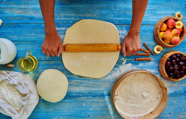 Top view of the girl rolls the dough on a blue vintage table, there are a number plate of mincemeat