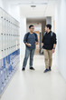 © selinofoto - Two students are standing next to lockers and talking together down the school hall. They are discussing a homework.