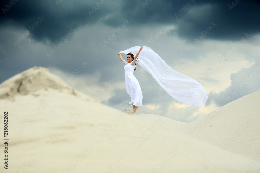 Piękna dziewczyna w białej sukni ślubnej z długim welonem na piaszczystej wydmie. - obrazy, fototapety, plakaty 
