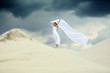 Piękna dziewczyna w białej sukni ślubnej z długim welonem na piaszczystej wydmie.