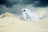 Fototapeta  - Piękna dziewczyna w białej sukni ślubnej z długim welonem na piaszczystej wydmie.