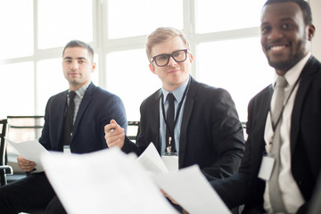 Wall Mural - Adult multiracial men in suits sitting with papers in hands and communicating on business meeting