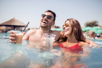 Wall Mural - Happy young couple drinking lemonade in swimming pool