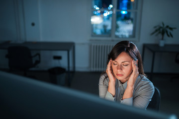 Tired and exhausted young woman sitting in front of computer screen at night.