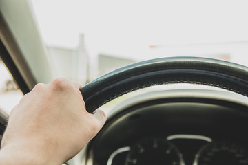 The man is sitting in the car, holding his hand on the steering wheel. The concept of driving a car, moving the wheel of a car.