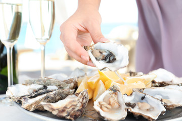 Woman holding fresh oyster over plate, focus on hand