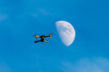 A Consumer Quadcopter Camera Drone Hovering With A Blue Sky And The Moon Behind
