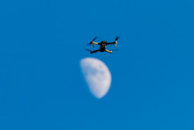 A Consumer Quadcopter Camera Drone Hovering With A Blue Sky And The Moon Behind