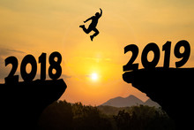 Happy New Year Silhouette Sunset Background. A Man Jumping Over Cliff And Jump Between 2018 And 2019 Years. Photo Silhouette And New Year  Concept Idea.