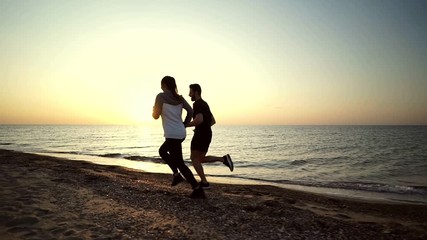 Poster - Side view of Young sports couple running toogether on beach near the sea