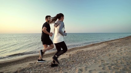 Canvas Print - Side view of Attractive sports couple running and having fun together on beach near the sea