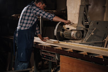 Side View Of Carpenter Using Saw At Wooden Workshop