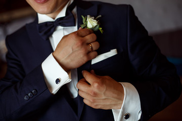 stylish man in black suit and white shirt corrects the boutonier. the groom hands with a boutonier close up portrait  . meeting of the groom.