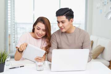 Beautiful young business woman and handsome businessman in formal suits are using gadgets, talking and smiling while working in office