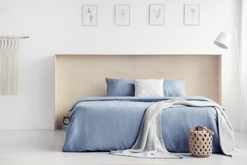 Wall Mural - Blanket and pillows on blue bed in white minimal bedroom interior with posters and lamp. Real photo